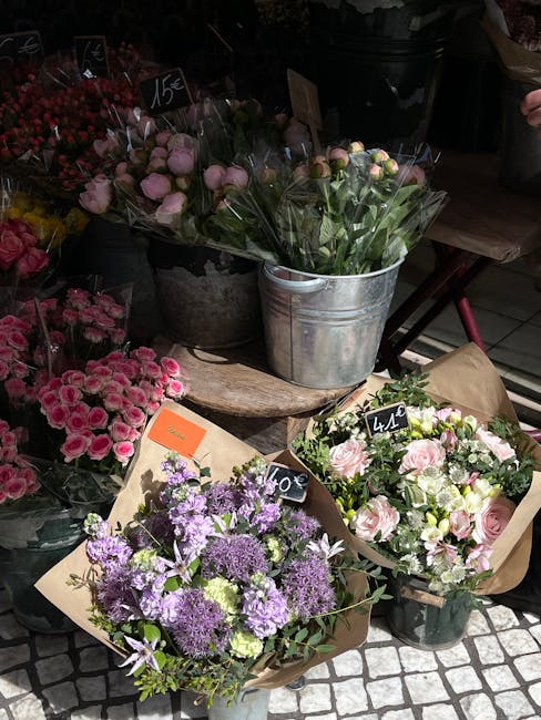 A display of fresh flower bouquets at a florist shop, featuring a variety of arrangements. One bouquet in the foreground contains purple, lavender, and white flowers, including alliums and astilbes, w